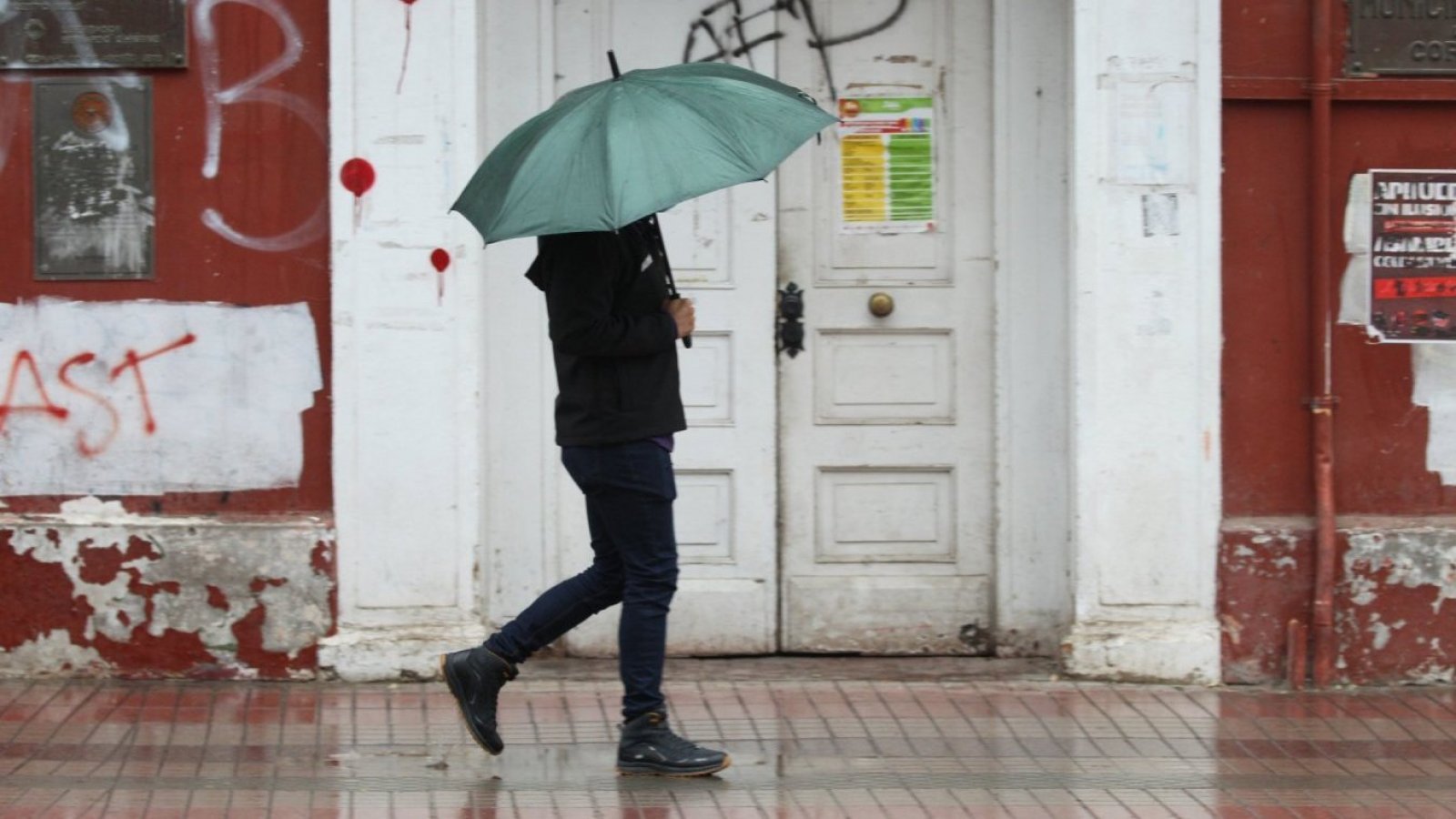 Persona caminando bajo la lluvia con un paragua verde.
