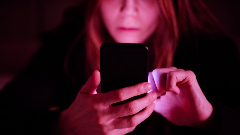 Una mujer envía un mensaje de texto en la oscuridad