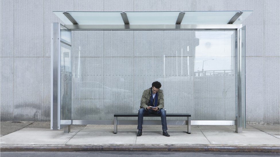 Un hombre mira su telefono solo en una estación de bus