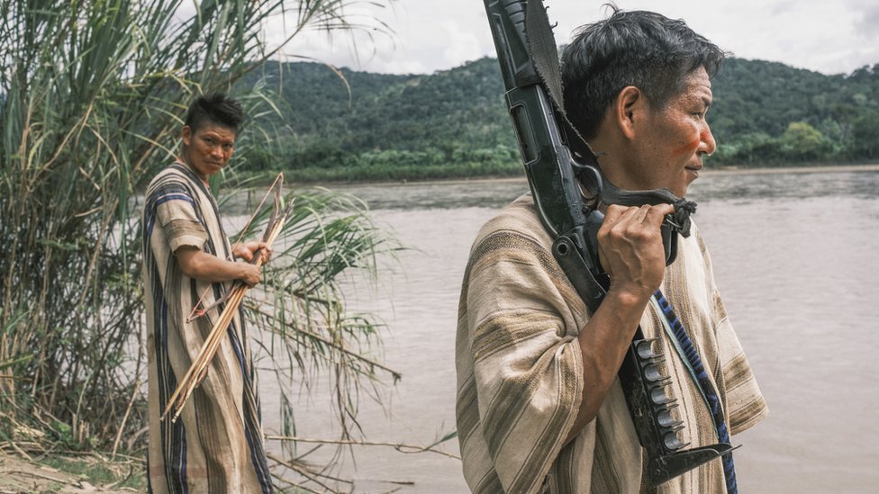 Dos hombres de los comités patrullan un río en el VRAEM