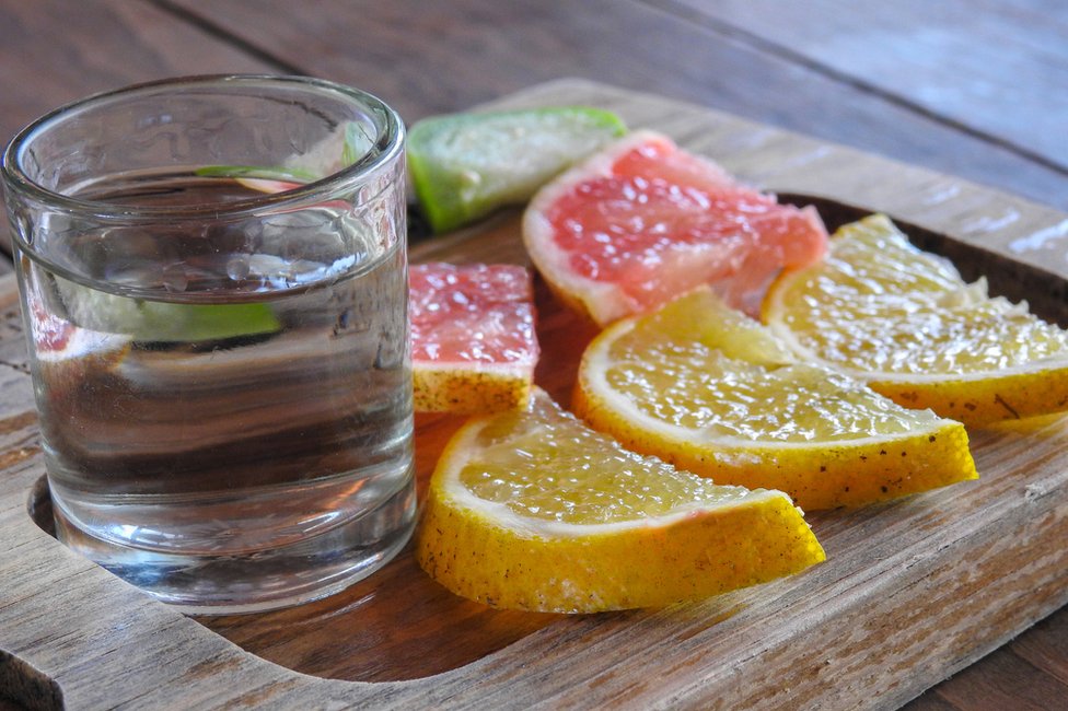 Shot de destilado con pedazos de fruta al lado.