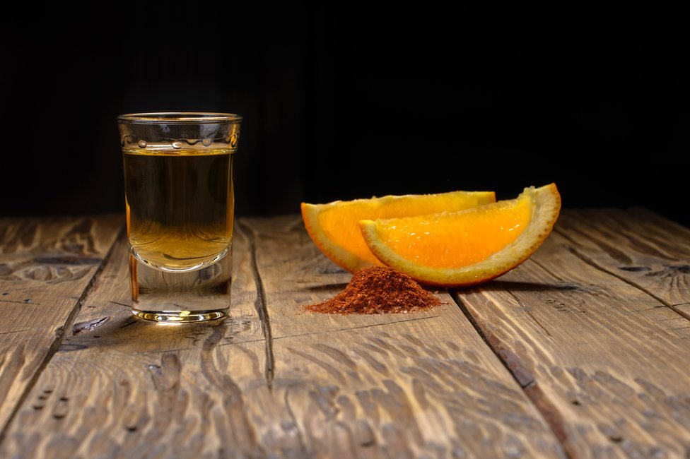 Shot de destilado reposado o añejo con dos pedazos de naranja.