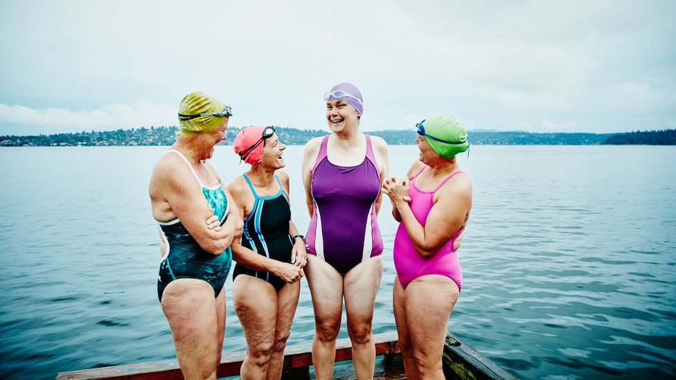 Cuatro alegres mujeres de mediana edad en vestidos de baño frente a un lago