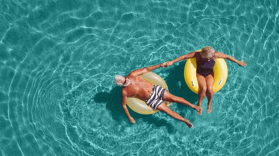 Una pareja de mediana edad tomando el sol sobre flotadores en una piscina