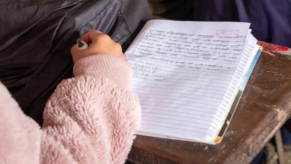 Una chica escribe en un cuaderno escolar en el idioma kusunda.