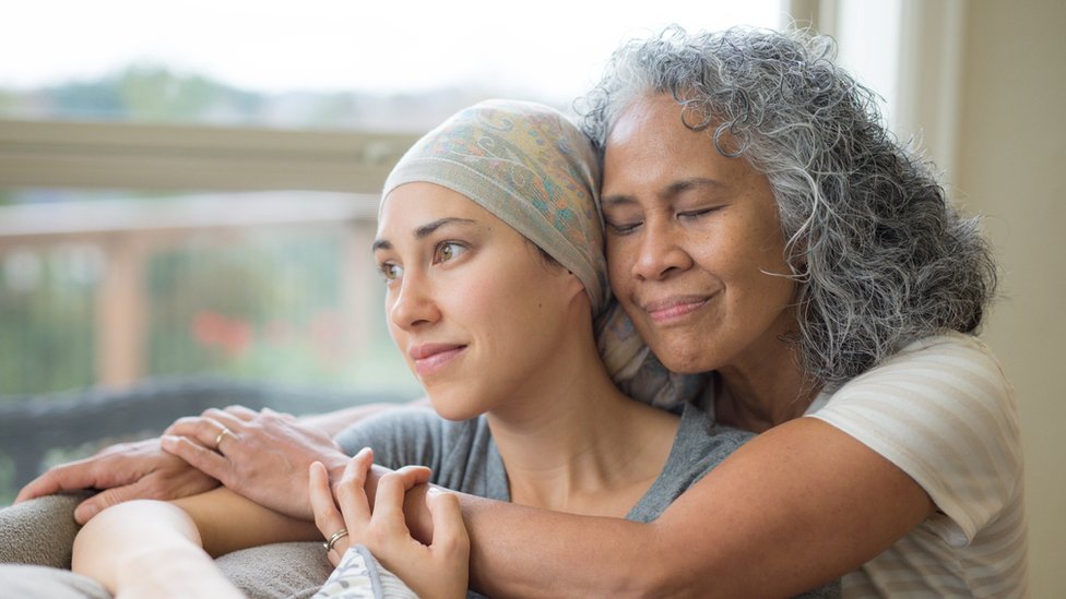 Mujer en sus 50 abrazando a su hija de alrededor de 20 años luchando contra el cáncer.