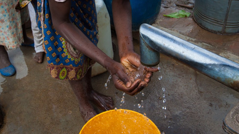 Una mujer recoge agua con sus manos de un pequeño chorro.