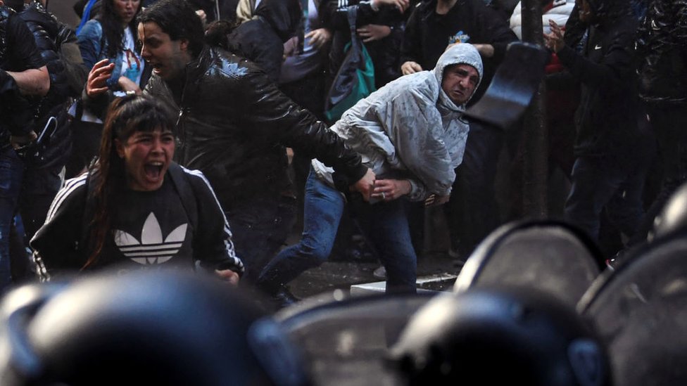 Una mujer grita frente a los antidisturbios, otro les lanza cosas. En primera línea de foto, los antidisturbios.