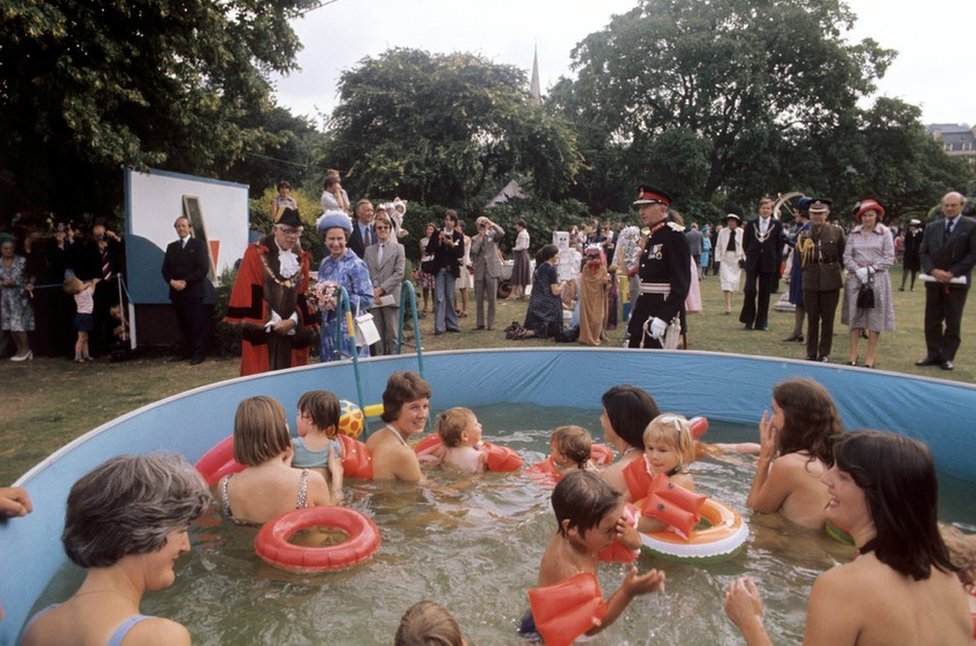 La reina Isabel II observa a personas en una piscina en Parade Gardens, Bath, durante su gira del Jubileo de Plata por Gran Bretaña.