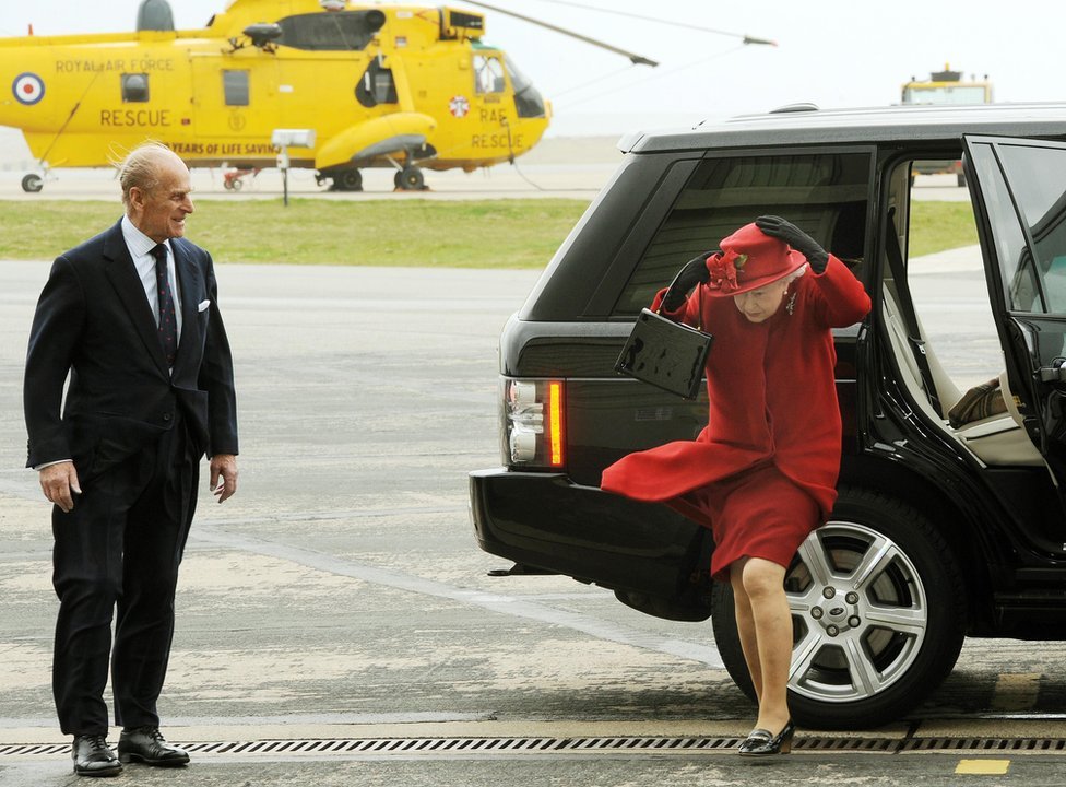 La reina Isabel II y el duque de Edimburgo llegan a un ventoso valle en Anglesey para visitar a su nieto, el príncipe Guillermo, en la base de la fuerza aérea.