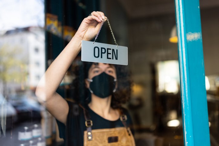 Una empleada coloca un letrero de "abierto" frente a un establecimiento.
