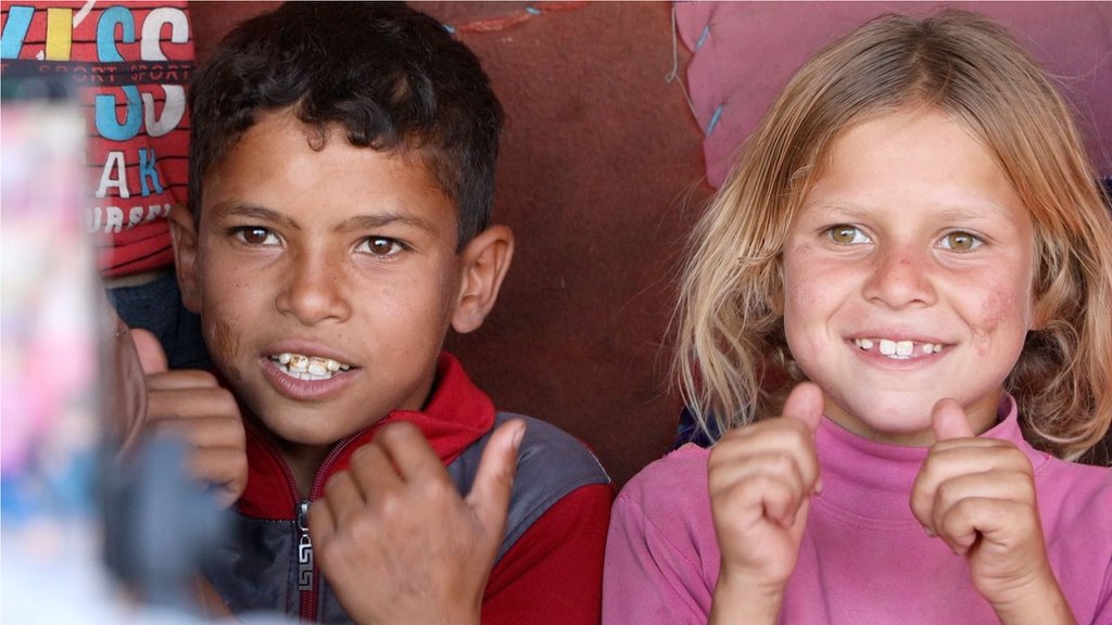 Un niño y una niña con sus pulgares levantados ante la cámara.