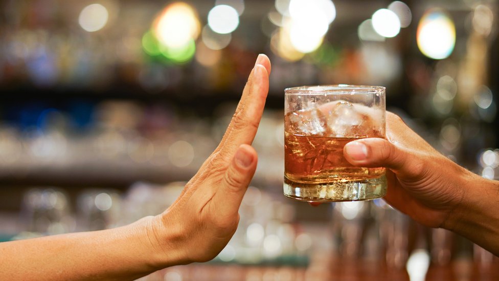 Una mujer rechaza un vaso de alcohol.