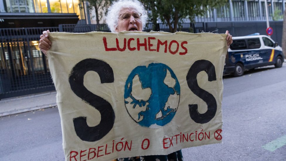 Una mujer sostiene una bandera con la leyenda: Luchemos. SOS. Rebelión o extinción