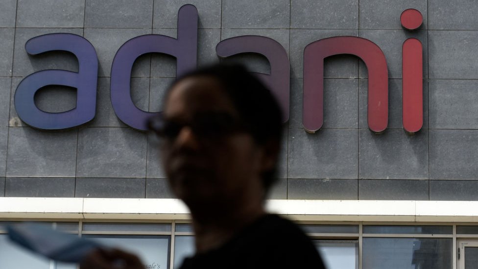 Una mujer pasando frente a un edificio con el lodo de Adani en Mumbai.