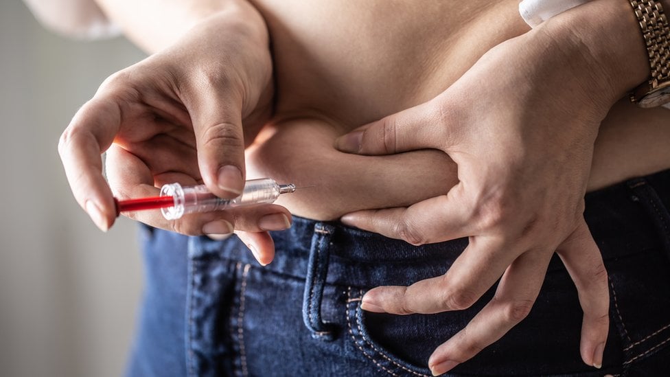 Una mujer se aplica una inyección en el abdomen.