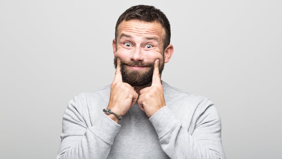 Un hombre forzándose a sonreír.