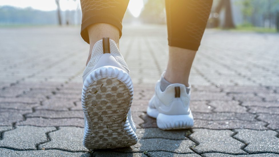 Primer plano de los pies de una persona con zapatillas deportivas caminando sobre una calle adoquinada.