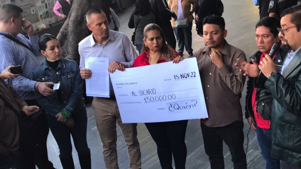 Flores sosteniendo un cheque simbólico sobre los 5.000 pesos que ofrecen por su vida.