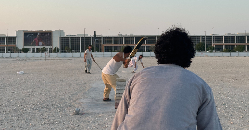 Migrantes jugando críquet frente en un descampado.