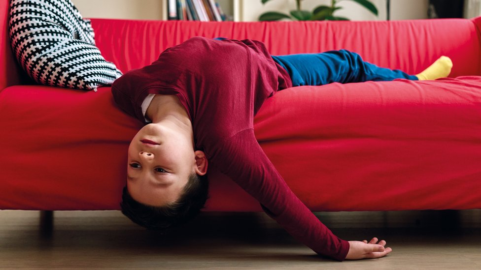 Niño aburrido tumbado al revés en un sofá