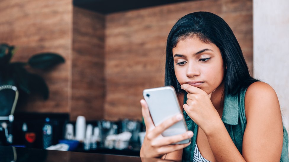 Una mujer mria con cara de preocupación su teléfono celular.