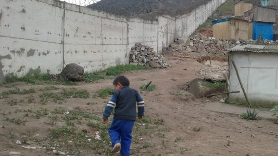 Un niño camina cerca del muro del lado donde se levantan casas humildes.