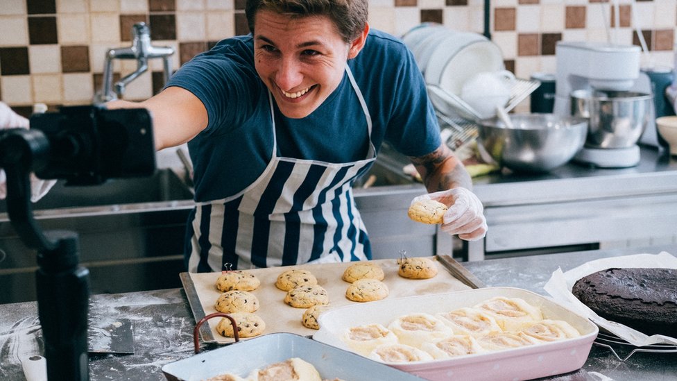 Un hombre se filma con su teléfono mientras hornea galletas.