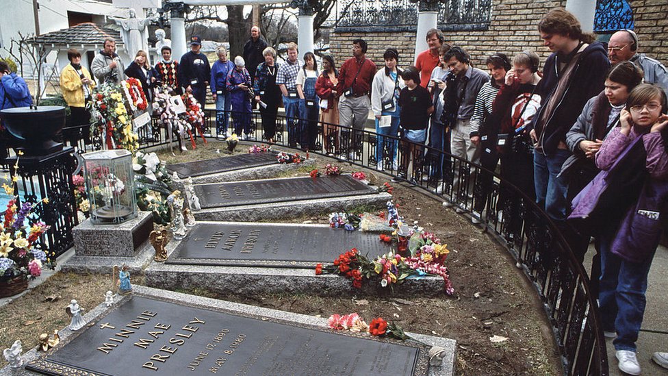 Fans se amontonan alrededor de la pequeña reja que los distancia de la tumba de Elvis, en el centro, rodeada de las de sus familaires.