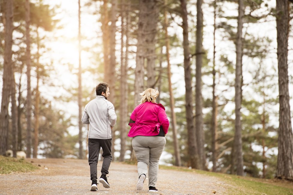 Mujer obesa y hombre delgado corriendo.