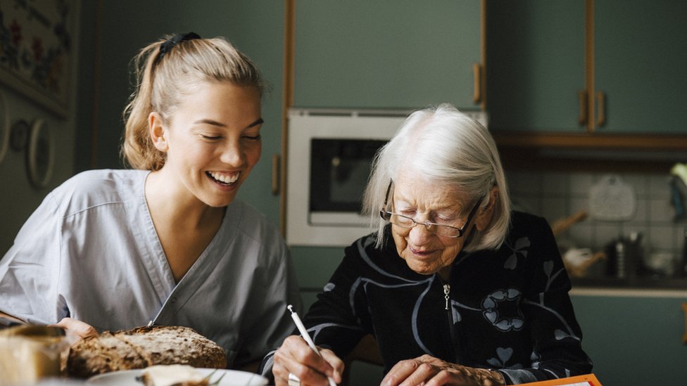 Una joven viendo a una anciana resolver un crucigrama.