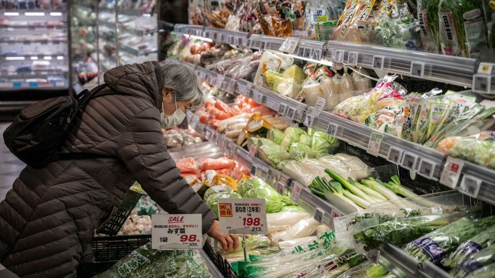 Una mujer se inclina frente a un refrigerador lleno de alimentos frescos.