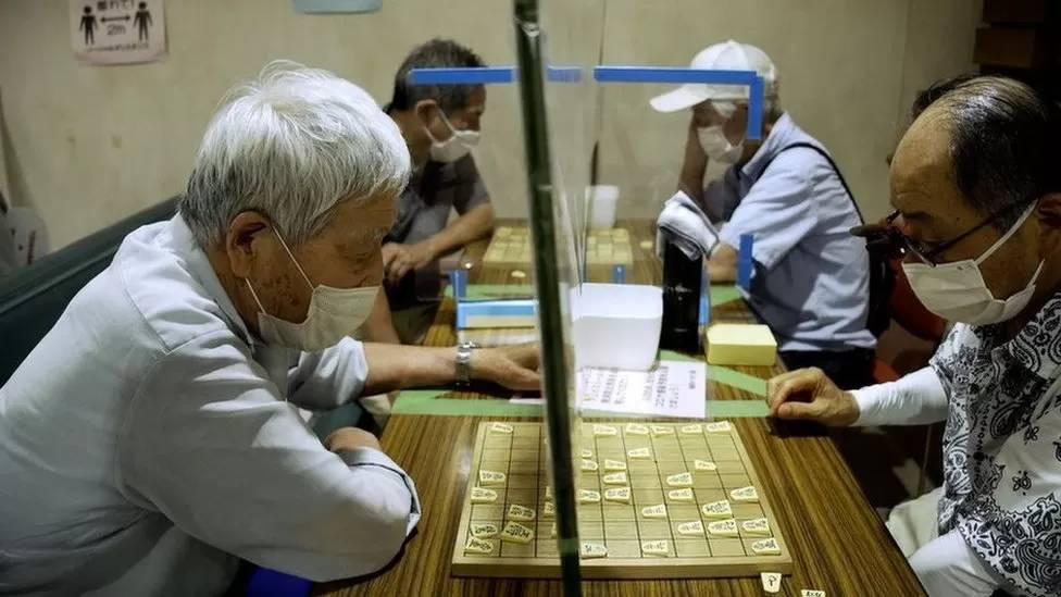 Varios hombres de muy avanzada edad, sentados, frente a frente, con un juego de mesa.