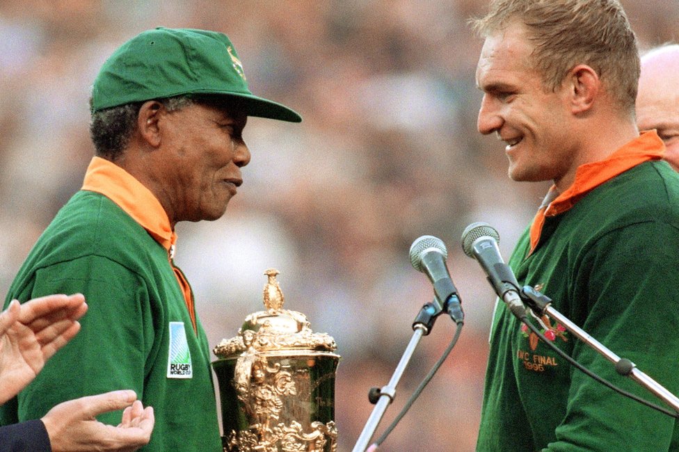 El presidente de Sudáfrica, Nelson Mandela, felicita al capitán de la selección sudafricana de rugby, François Pienaar, antes de entregarle el trofeo William Webb tras la victoria de su equipo sobre Nueva Zelanda (15-12) en la final de la Copa del Mundo de Rugby en Ellis Park, Johannesburgo, el 24 de junio de 1995.