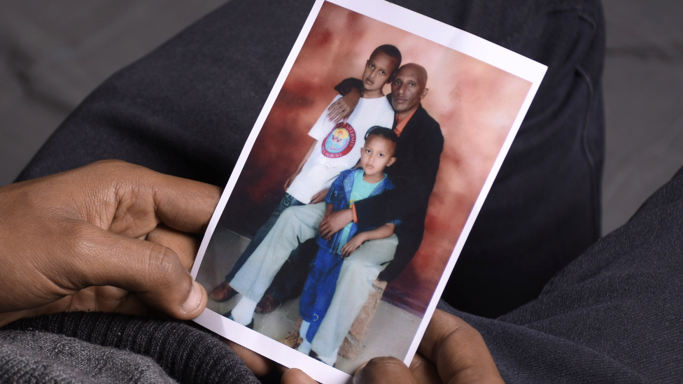 Moti Dereje con una vieja fotografía familiar de él y su hermano menor cuando eran niños con su padre.