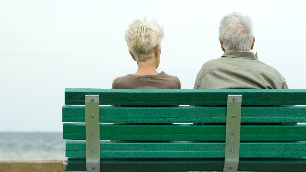 Un hombre y una mujer de espaldas sentados en un banco frente al mar