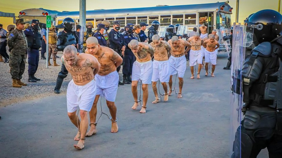 Prison agents observe gang members as they get off a bus at their arrival after 2000 gang members were transferred to the Terrorism Confinement Center