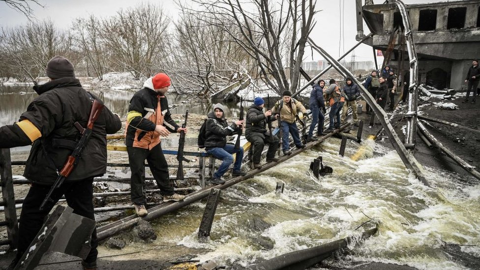 Miembros de la defensa civil cruzando un río donde el puente fue volado