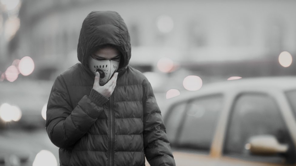 Una persona camina con un tapabocas en una ciudad contaminada.