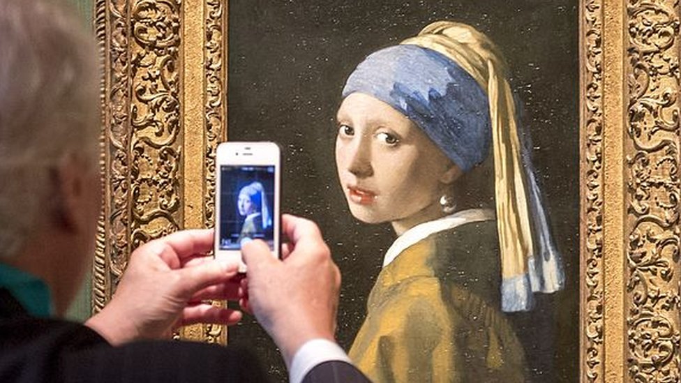 Un hombre toma una foto del cuadro La joven de la perla de Johannes Vermeer