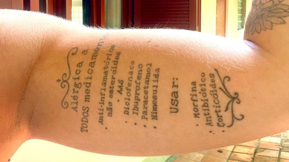Brazo de Amanda Munaretti Selbach con los nombres de los medicamentos a los que es alérgica tatuados.