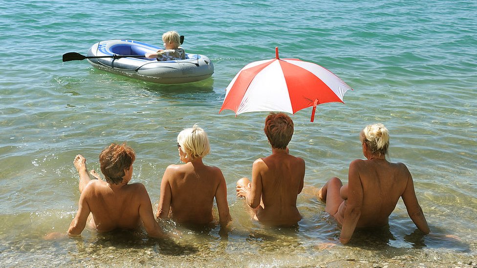 Mujeres desnudas tomando el sol a la orilla de un lago en Alemania observan a un niño en una balse