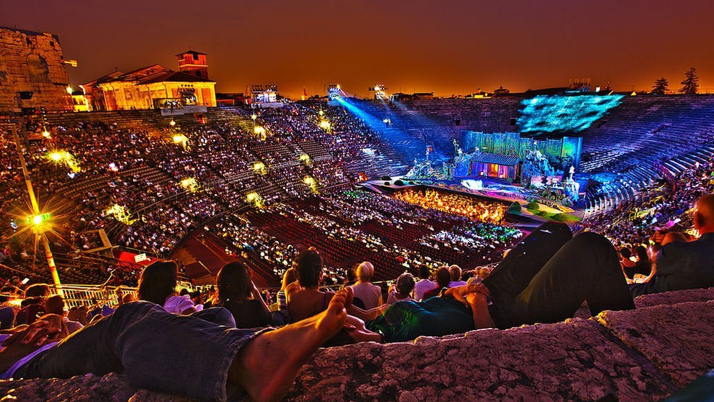 La ópera "Madame Butterfly" de Giacomo Puccini se toca en la Arena de Verona y los visitantes se relajan en los escalones de piedra. La famosa Arena di Verona es popular por el festival anual de ópera en verano.