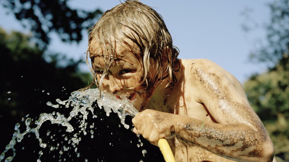 Un niño toma agua de una manguera