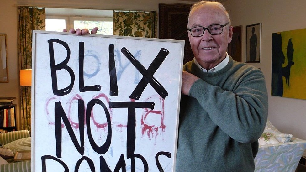 Una foto de Hans Blix sosteniendo un cartel que dice Blix y no bombas en 2013.