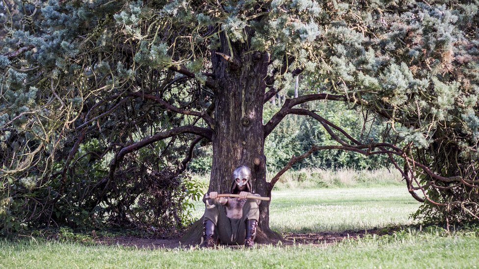 Un hombre vestido de vikingo sentando bajo un árbol.