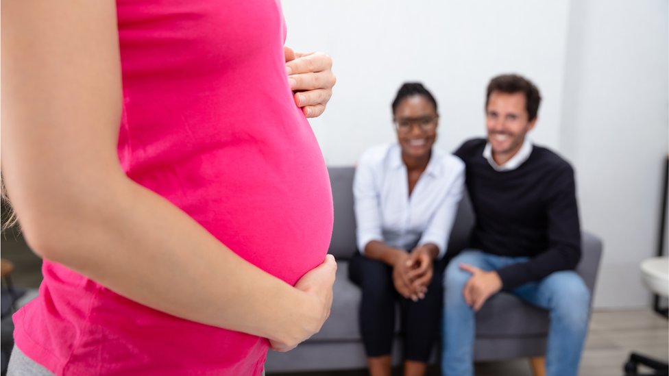 Una mujer embarazada frente a una pareja.
