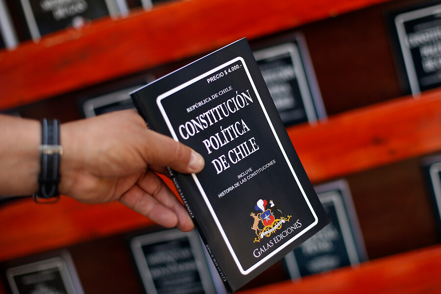 Mano sostiene un libro de la Constitución Política de Chile.