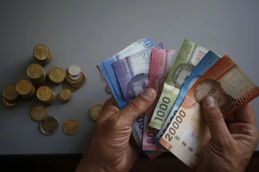 Persona sostiene billetes y monedas chilenas