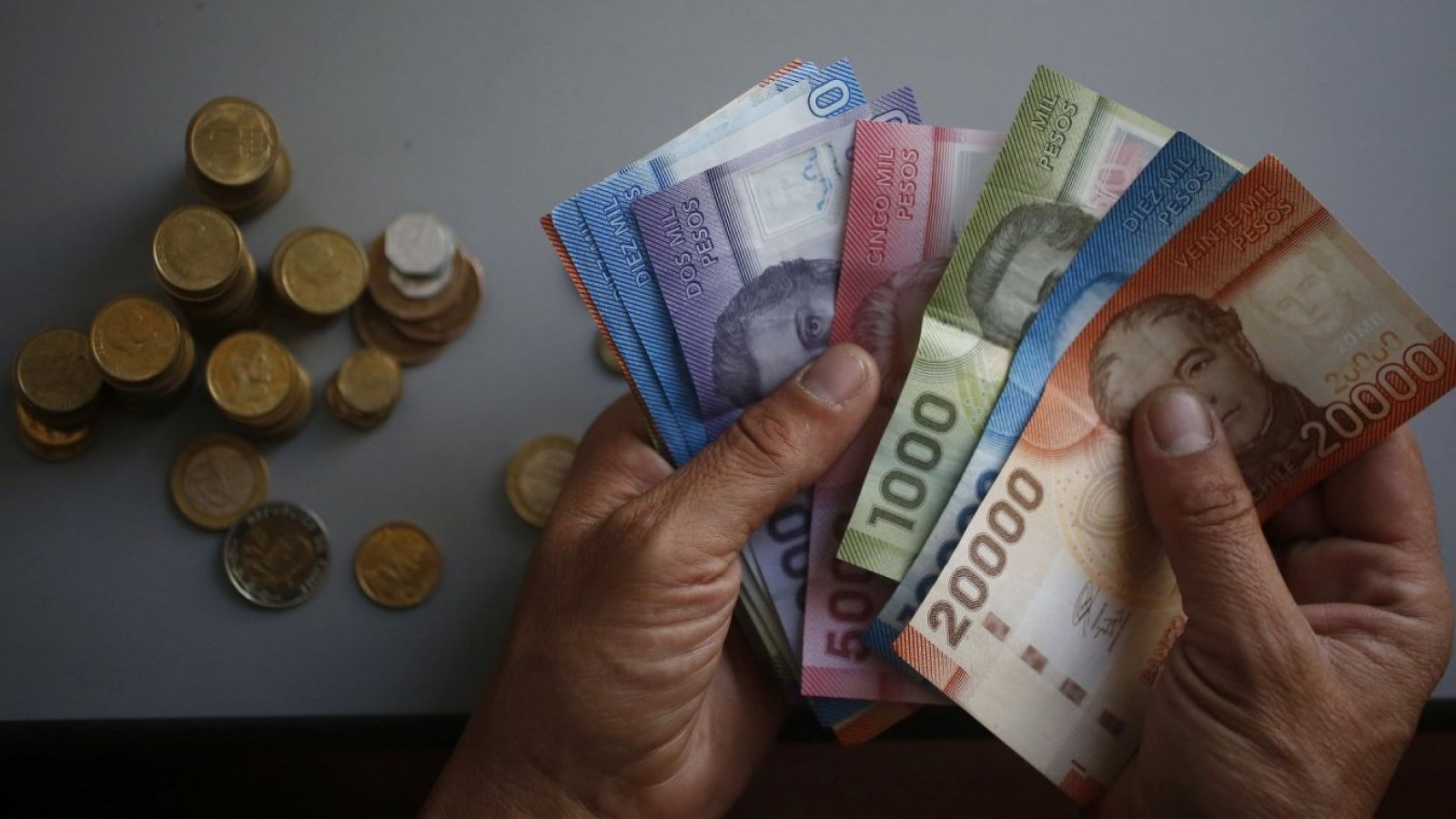 Persona sostiene billetes y monedas chilenas